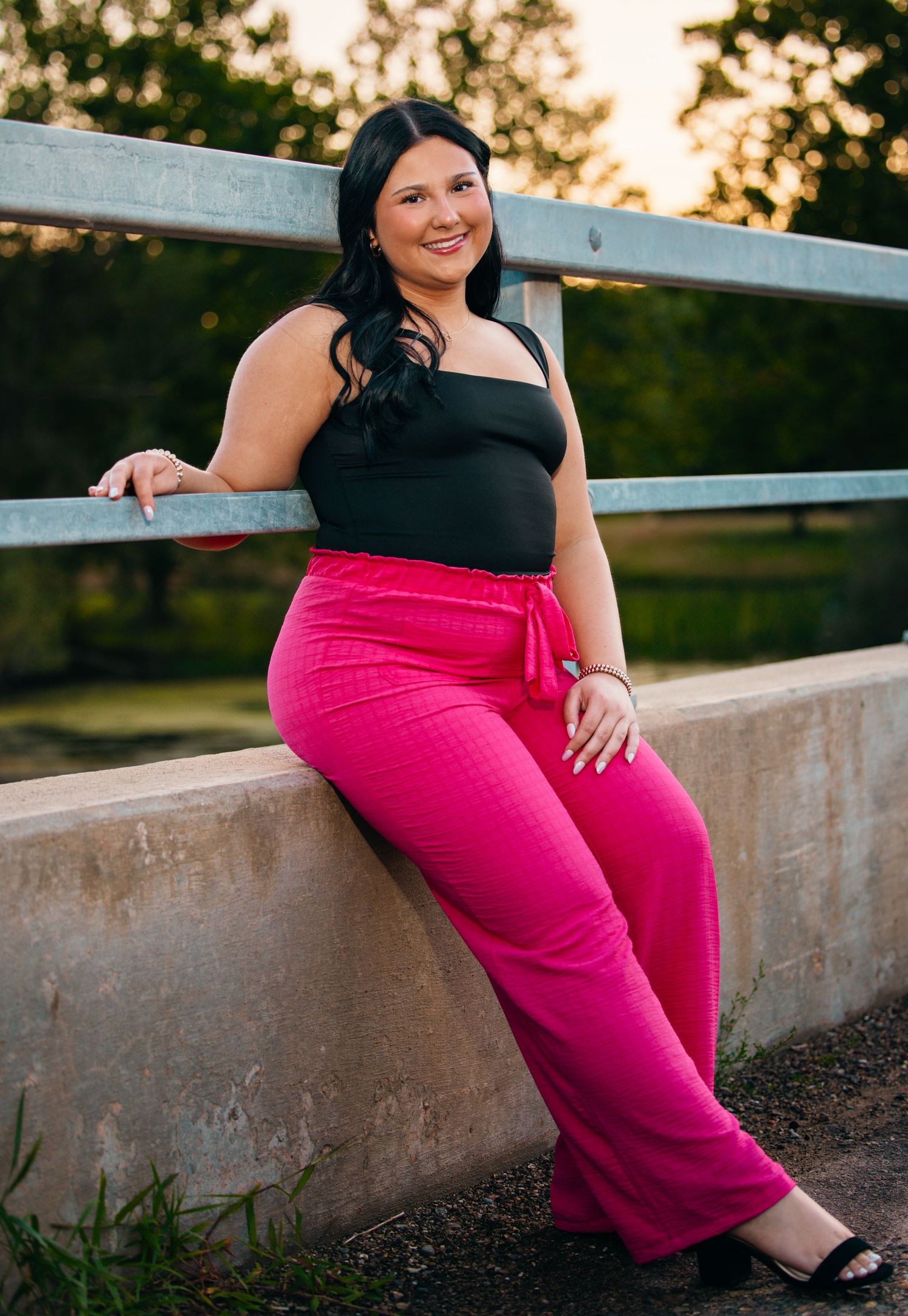 Portrait series on concrete wall wearing black top and bright pink pants at sunset.