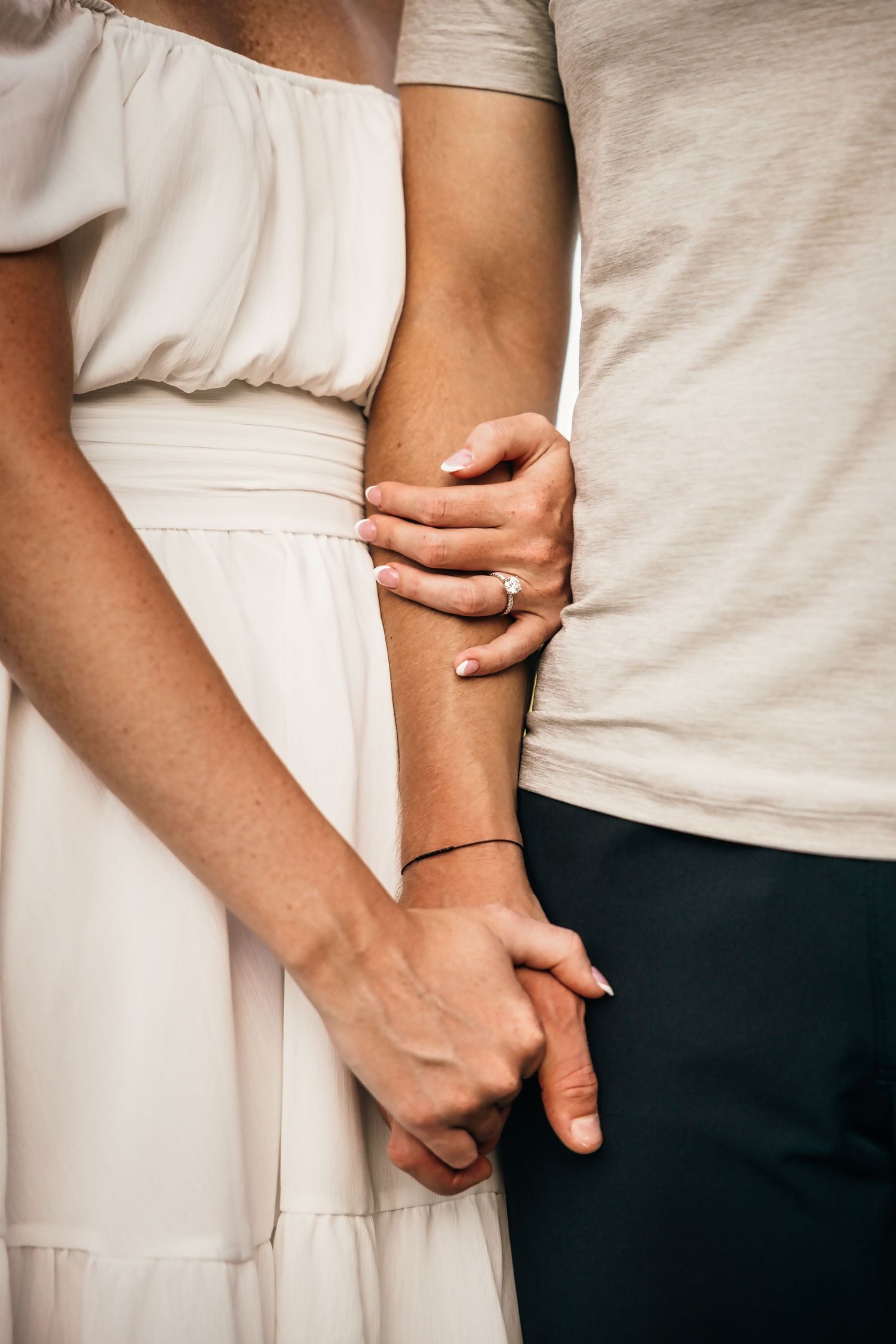 Close-up of hands embracing with a white dress and engagement ring visible.