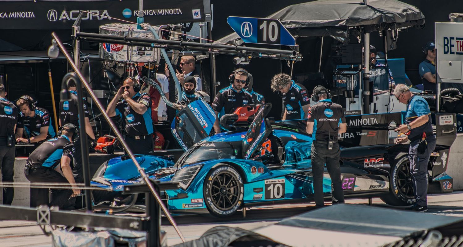 Racing pit crew and vehicles lined up in a professional motorsport garage environment.