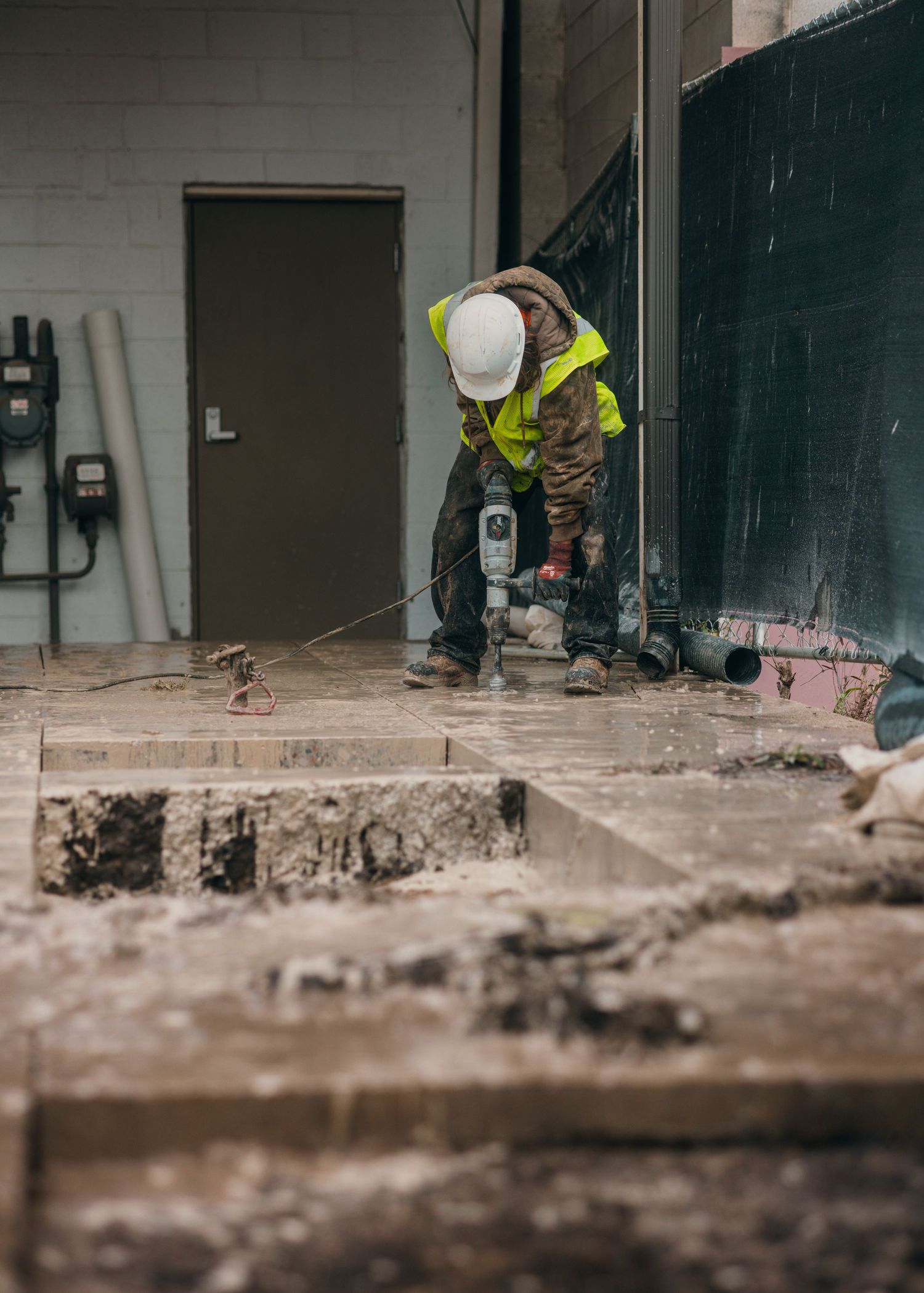 Construction worker in safety gear operating power tools on concrete floor.