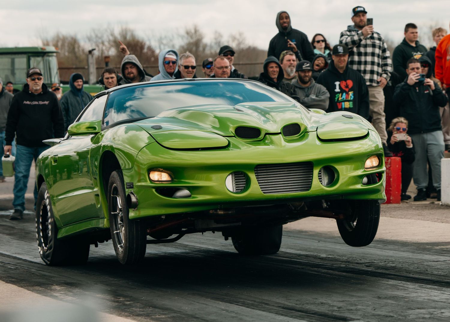 Lime green custom drag racing car in action on a race track with spectators watching.
