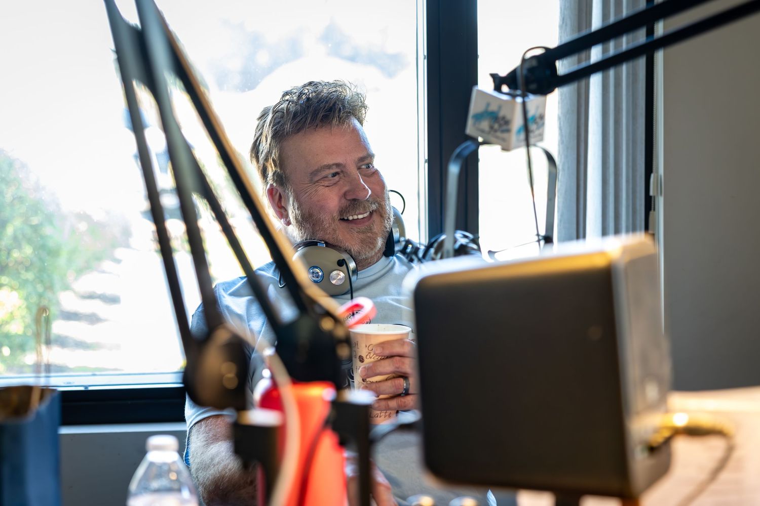 Person smiling while speaking into professional microphone setup in bright studio space.