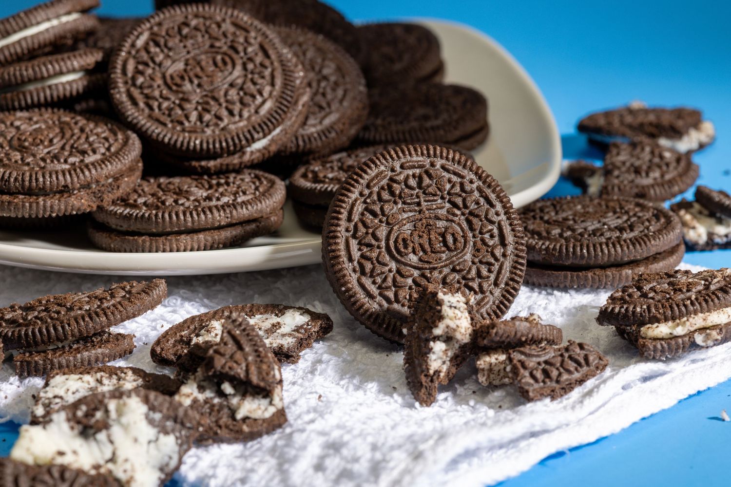 Stack of chocolate sandwich cookies scattered on white surface with crumbs.
