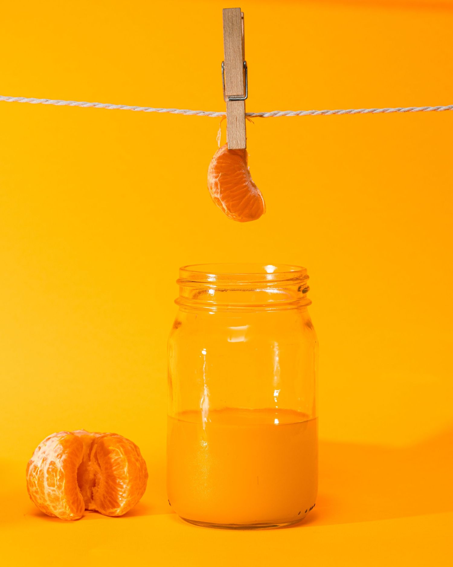 Creative orange-themed photo with mandarin segment hanging over jar of juice.