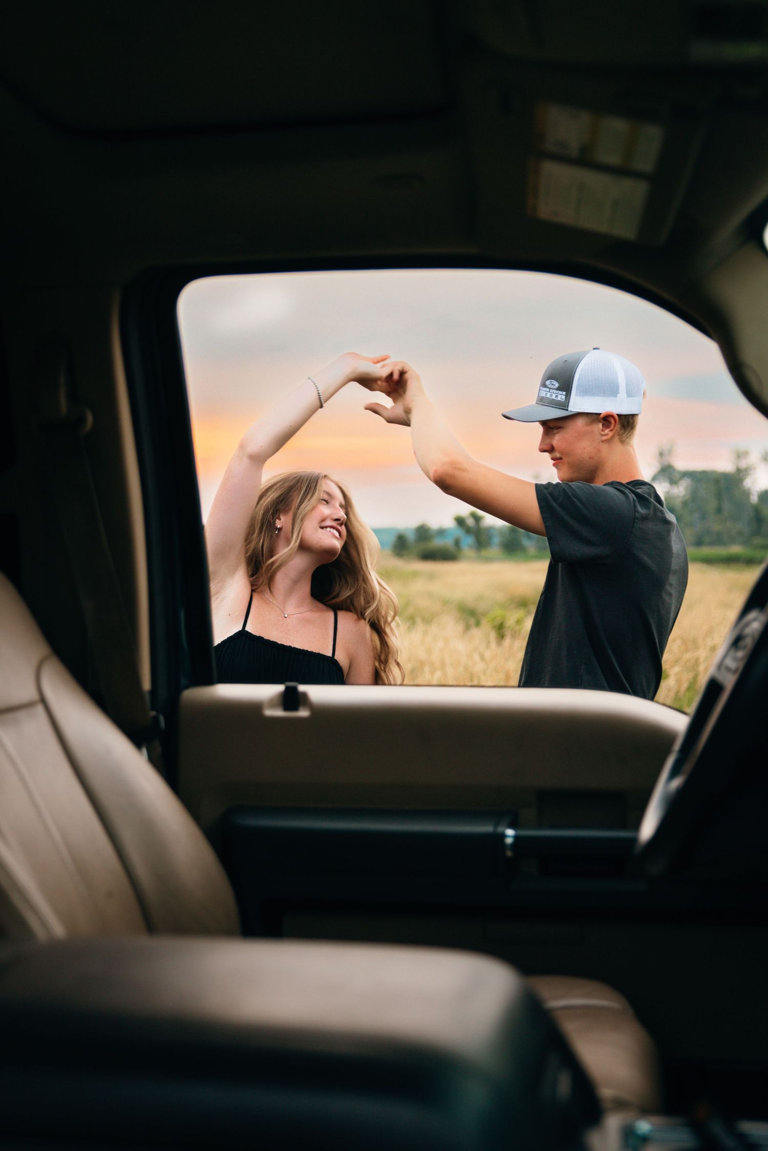 View through car window of couple enjoying moment together in field at sunset.
