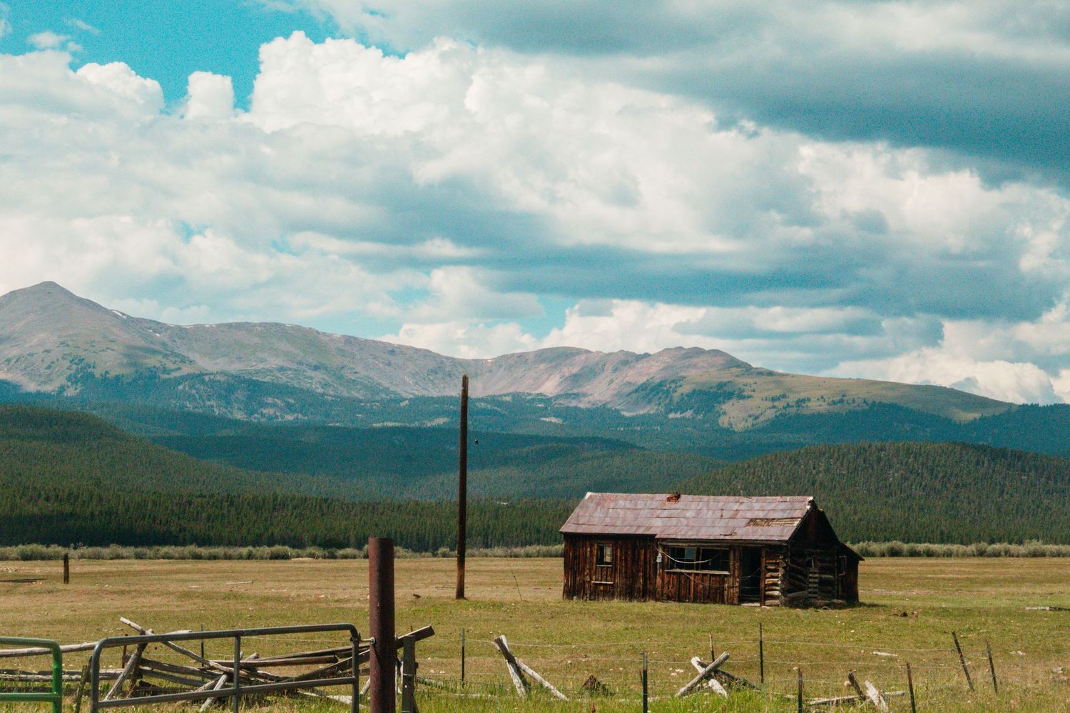 Mountain landscape with rustic barn and wooden fences stretching across open prairie.