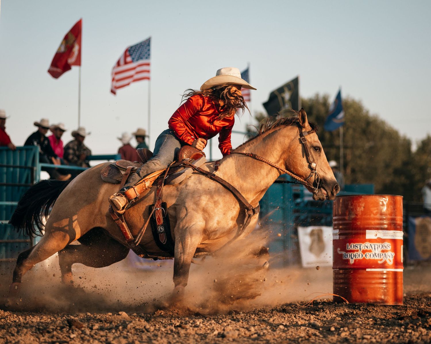 Barrel racer speeds around orange barrel during competitive rodeo event.