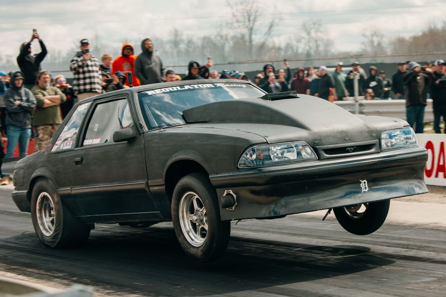 Drag racing car performing wheelie on track during competition event.