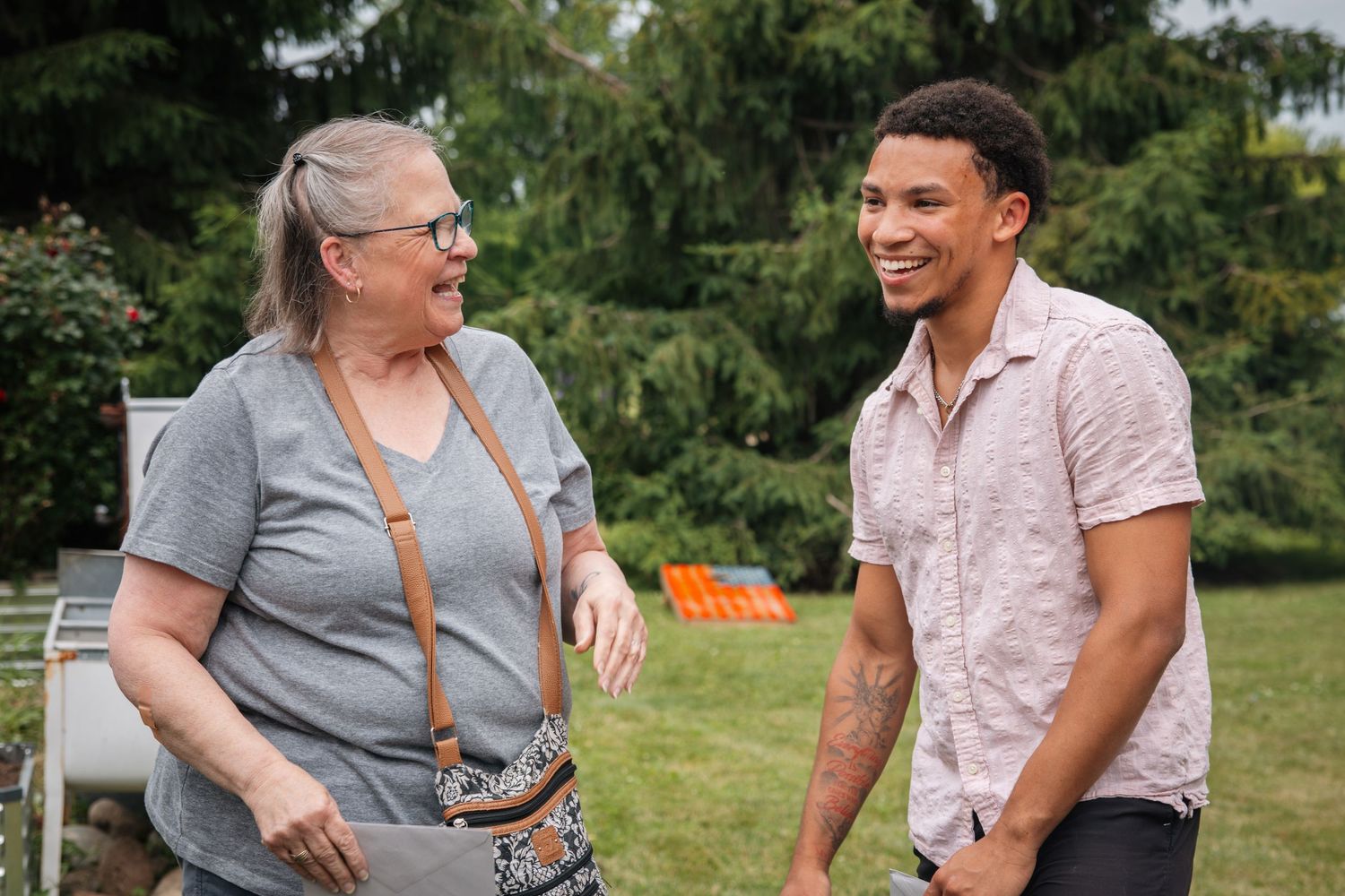 Two people having animated conversation outdoors on sunny day with trees in background.