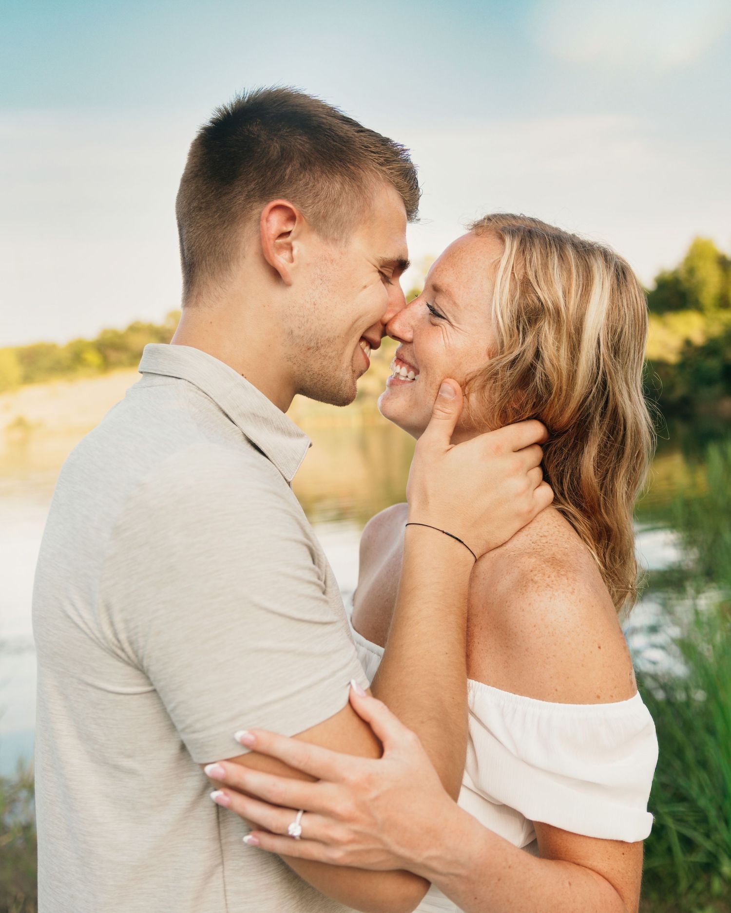 Romantic outdoor portrait of a couple sharing an intimate moment by a lake at sunset.