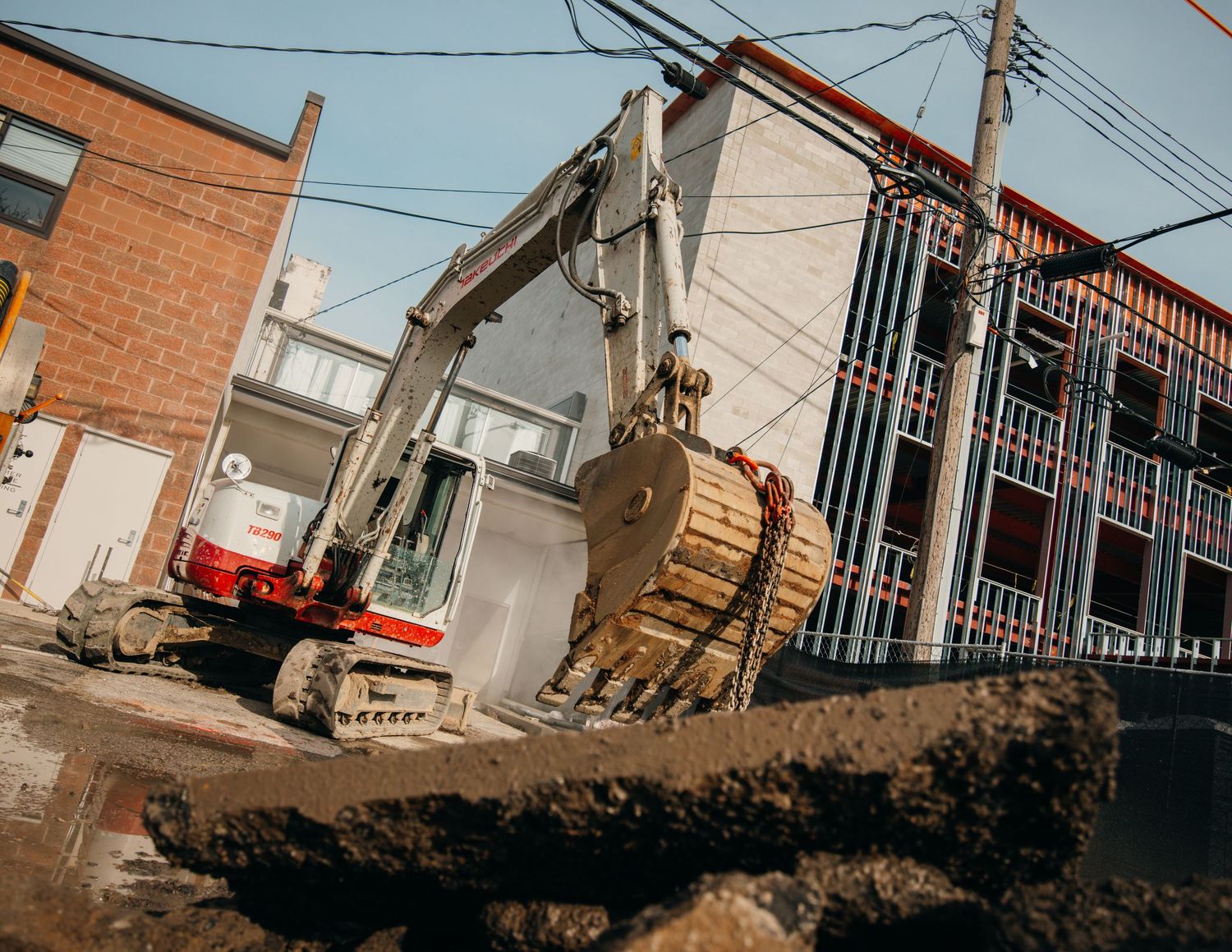 Construction or excavation site with power lines and buildings in background.