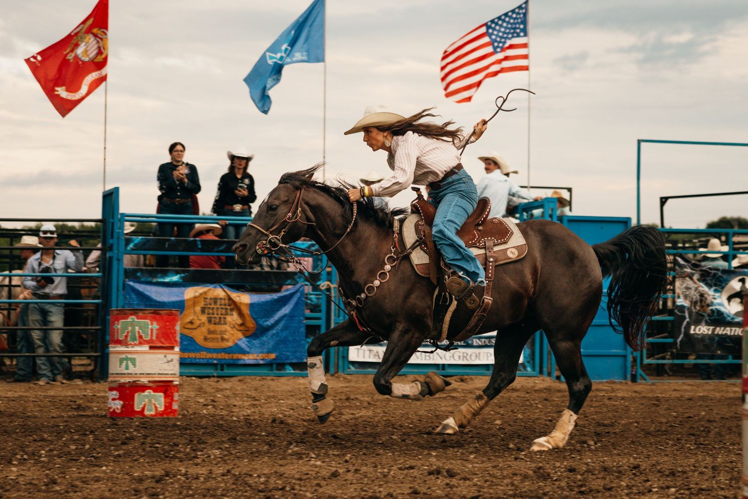 Multiple flags wave over a rodeo arena during a western competition event.