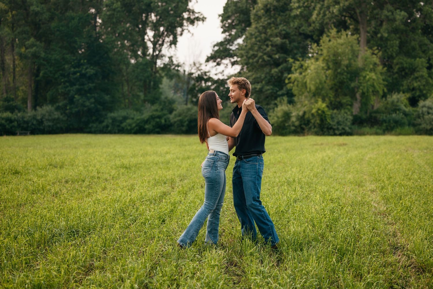 Couple dancing together in a sunlit meadow surrounded by trees.