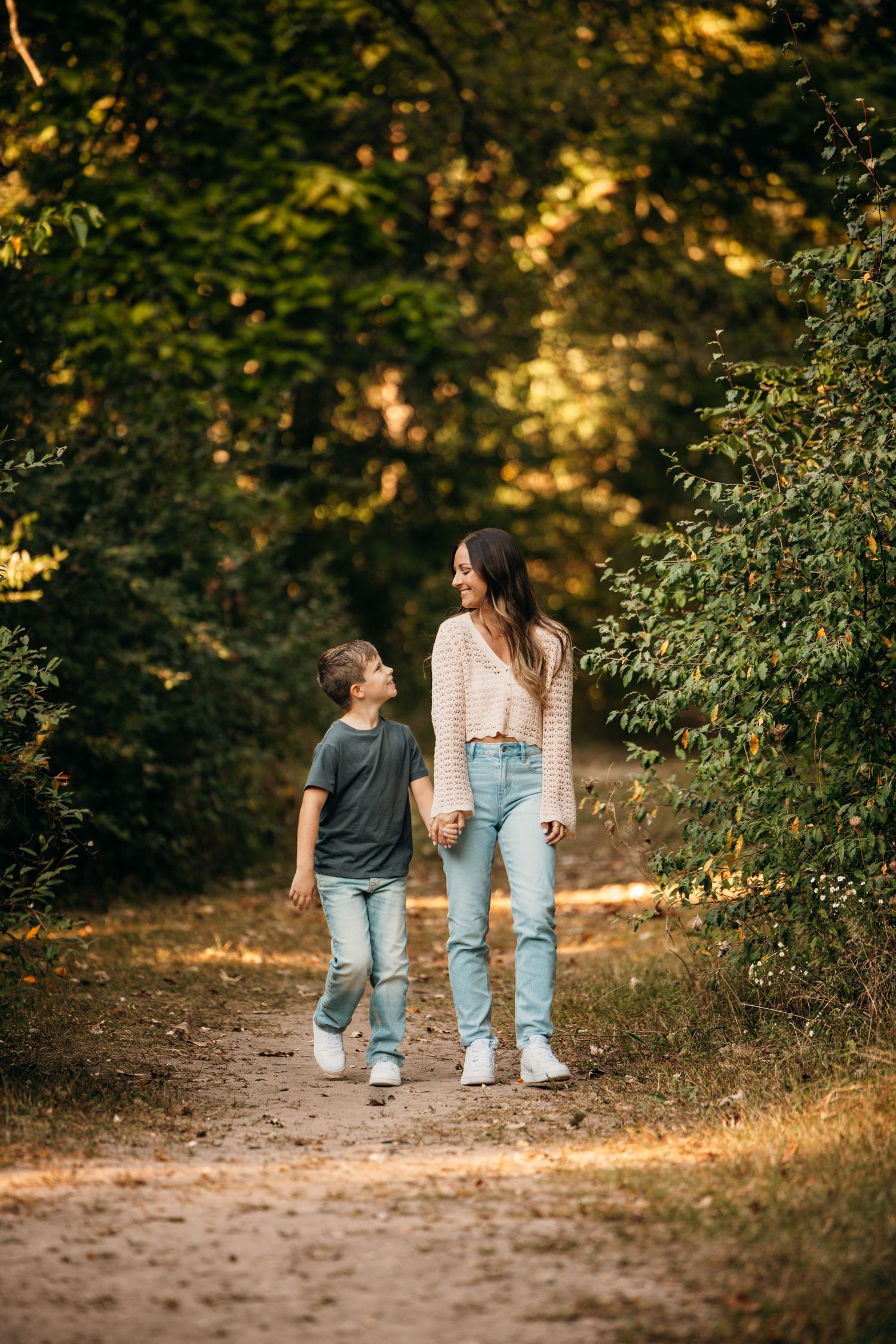 Two people walking together on an autumn forest trail with golden sunlight filtering through trees.