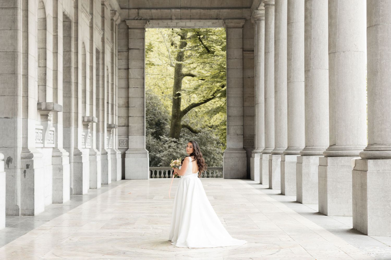 Mariée sous une architecture majestueuse, séance photo mariage civil Belgique, composition élégante, robe fluide et ambiance poétique
