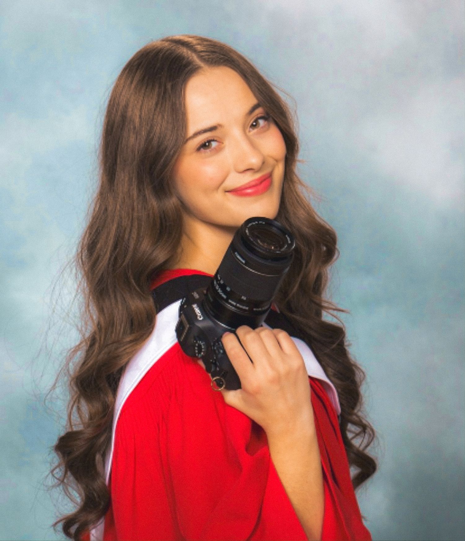 Photo of business owner in Graduation cap and gown holding camerfa