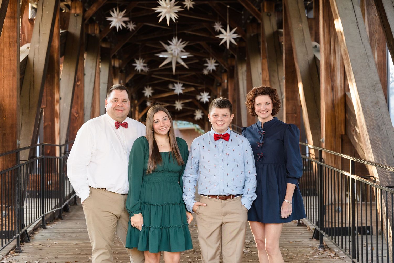 Wedding party group photos under decorative star lights in rustic wooden covered bridge.