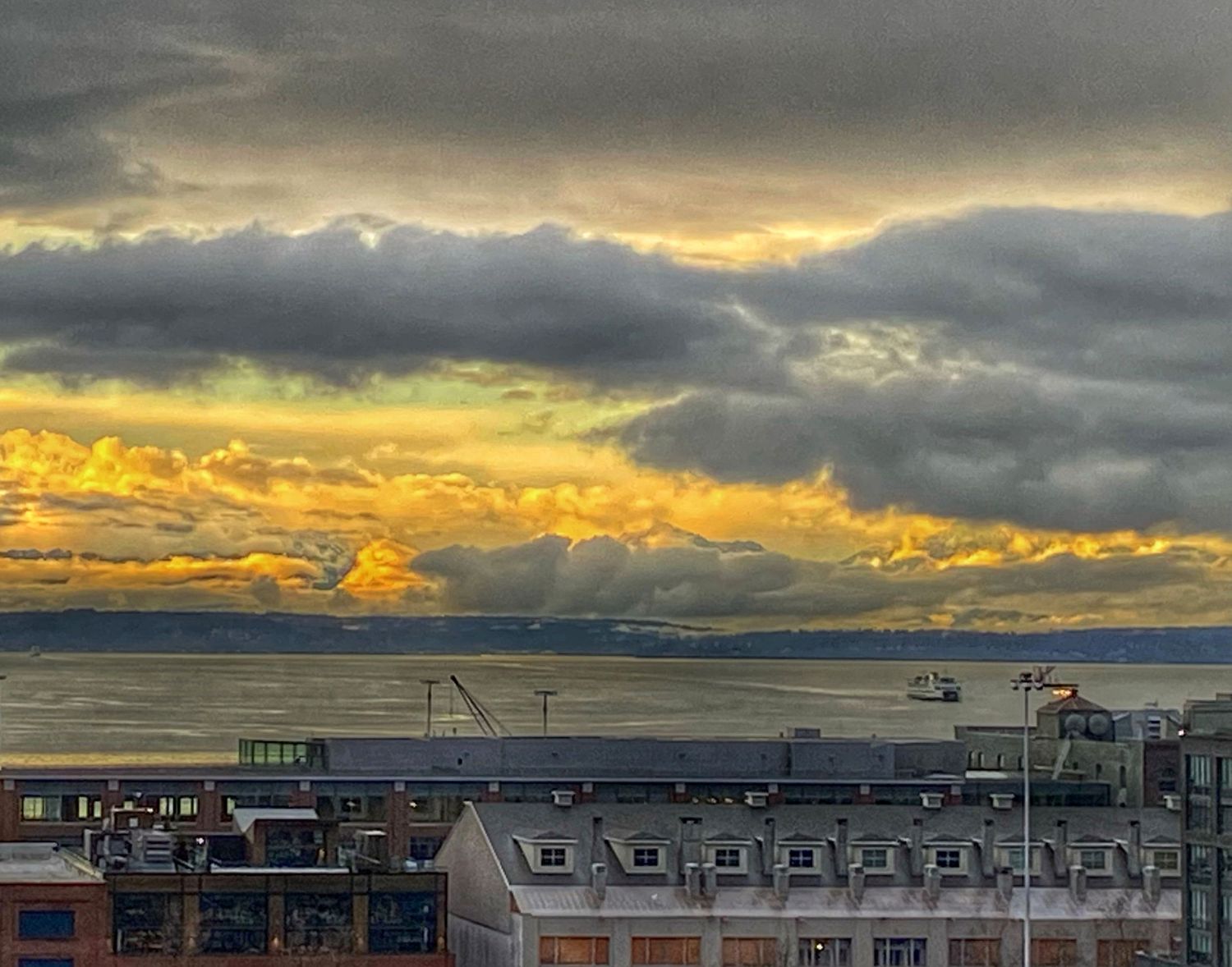 Dramatic sunset sky over residential rooftops with dark storm clouds and golden light.