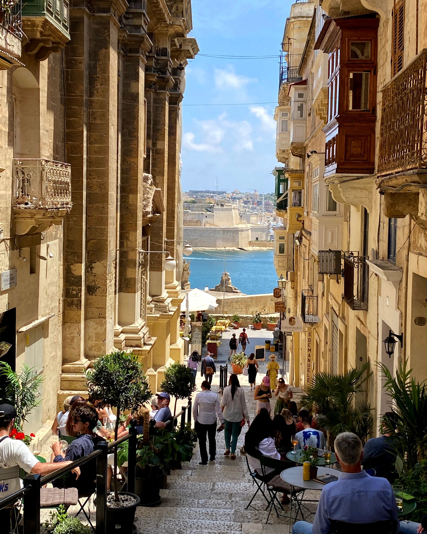 Historic stone archway corridor with outdoor seating overlooking a Mediterranean harbor view.