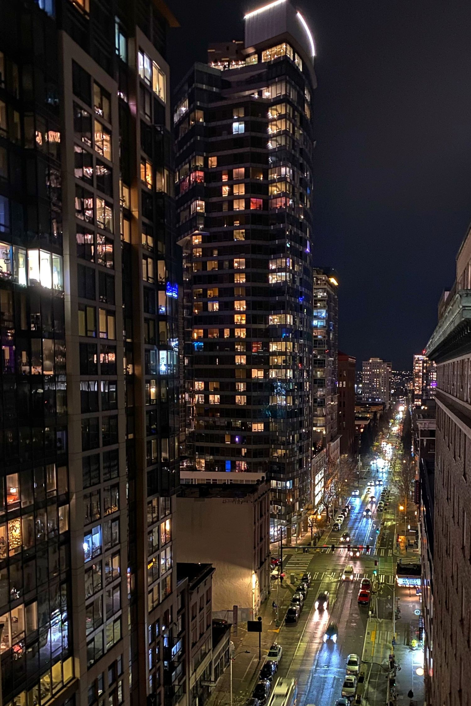 Illuminated high-rise buildings and city street at night with glowing lights and traffic trails.