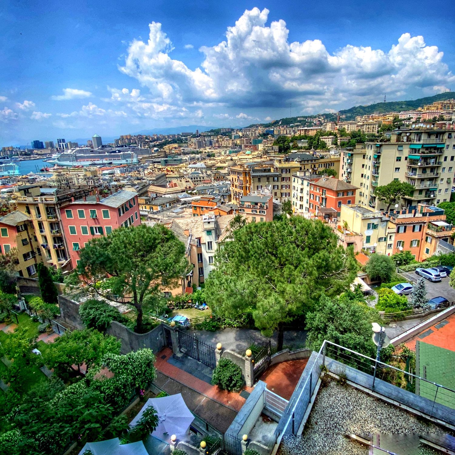 Panoramic cityscape view of colorful buildings and rooftops in Genoa, Italy under blue sky with white clouds.