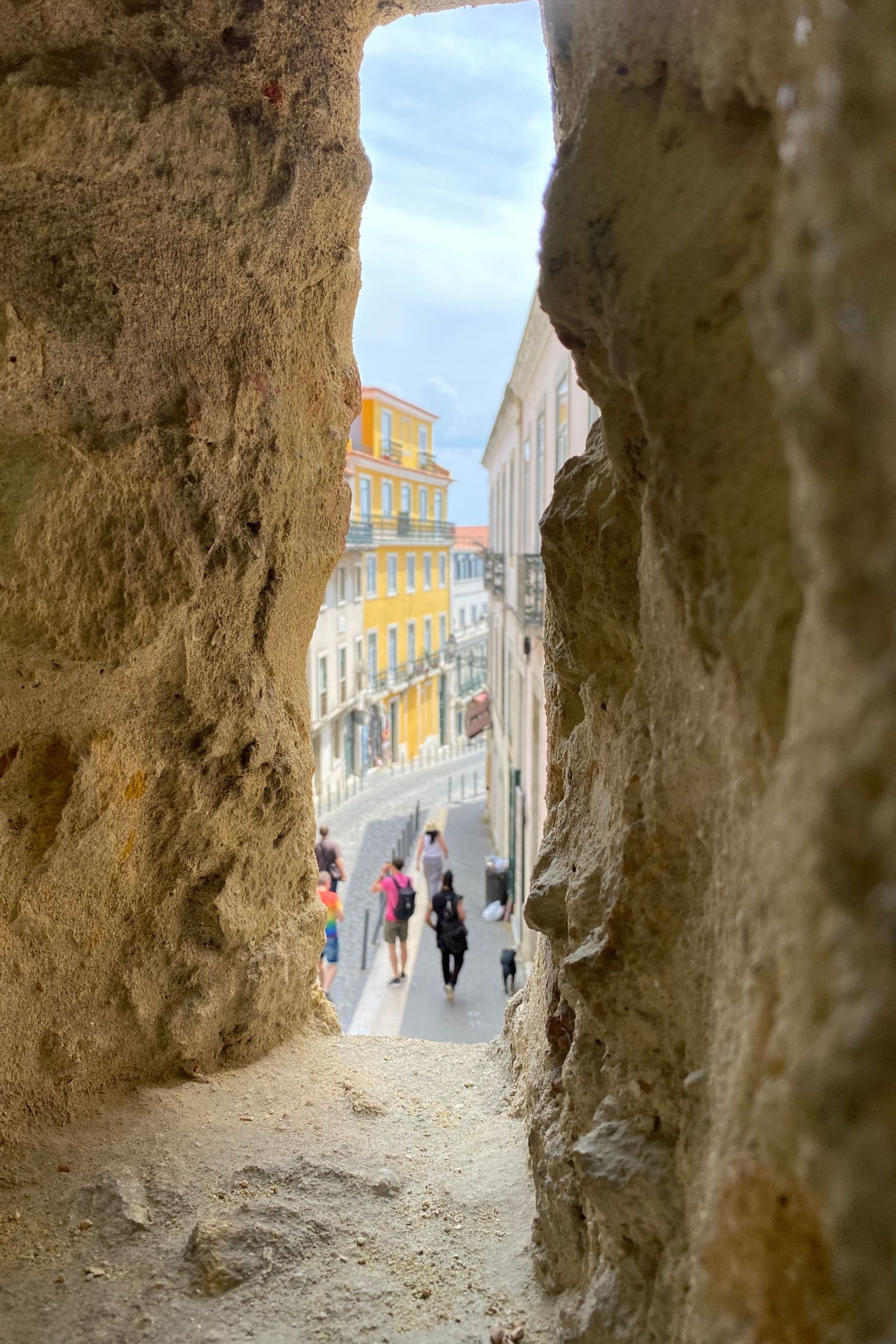 View through a stone passageway revealing a colorful European street scene.