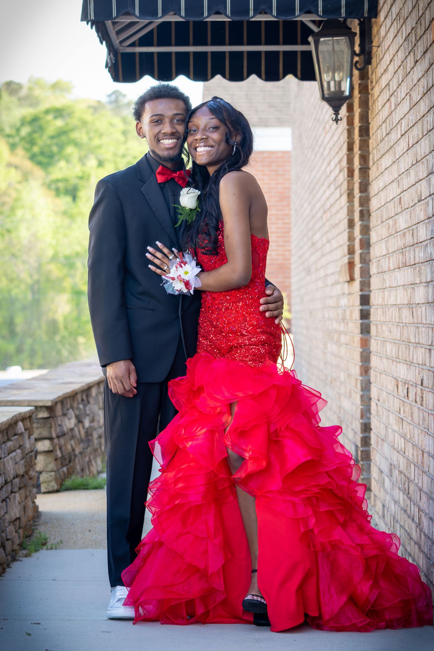 Couple in formal attire pose together, with woman wearing dramatic red ruffled gown.