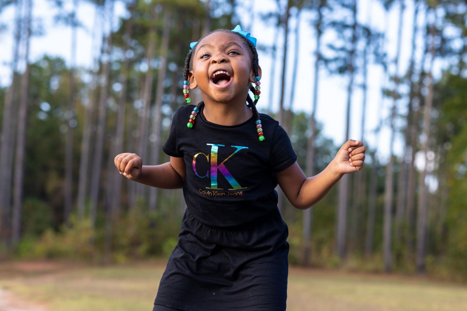 Child in black t-shirt laughing joyfully outdoors with pine trees in background.