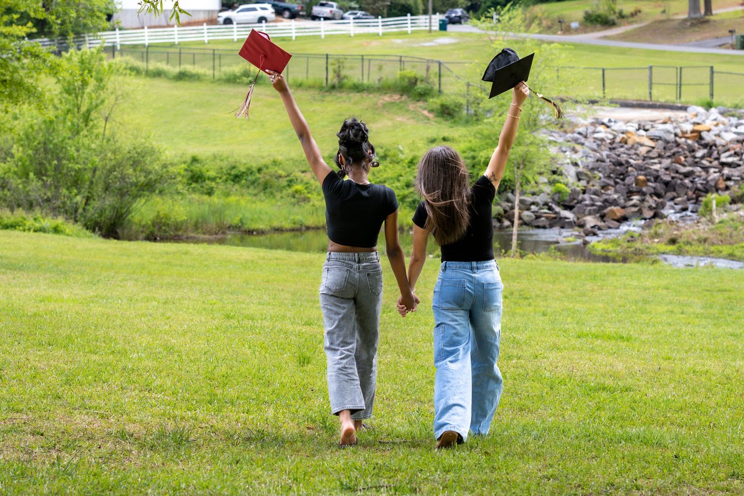 Two graduates holding caps and a diploma walk hand-in-hand across green grass, celebrating their achievement outdoors.