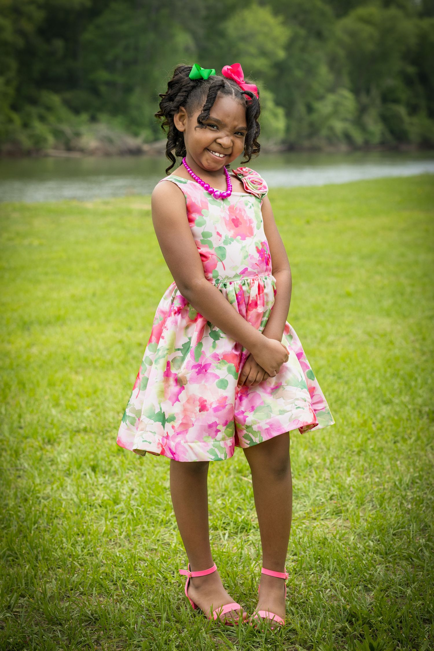 Child wearing floral pink dress and matching socks plays on green grass.