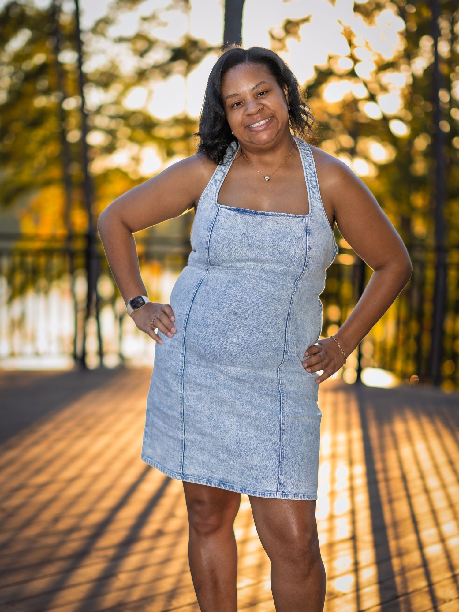Woman in denim dress poses confidently at sunset with long shadows on pavement.