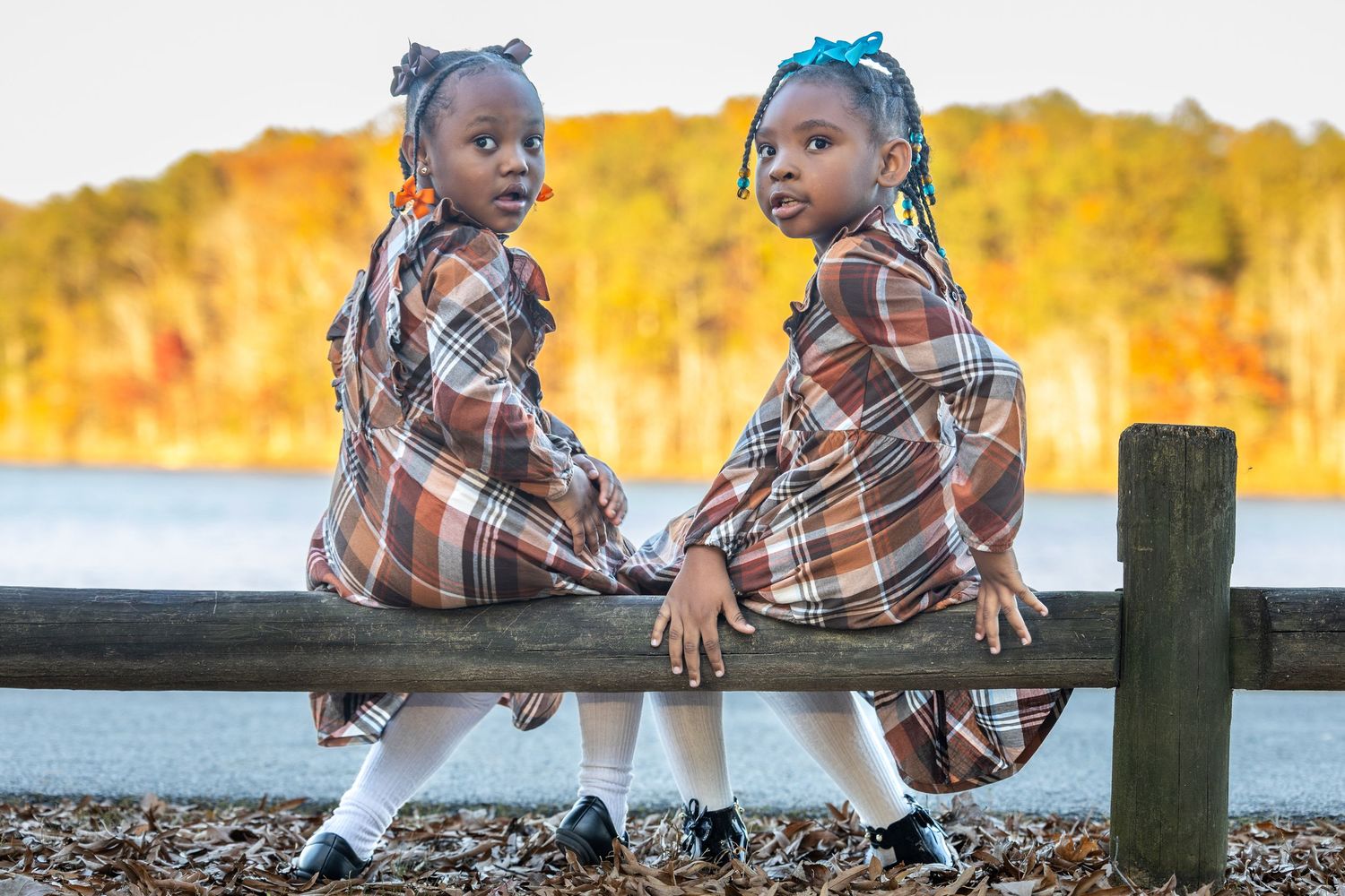 Kids in matching outfits posing on wooden fence at sunset.