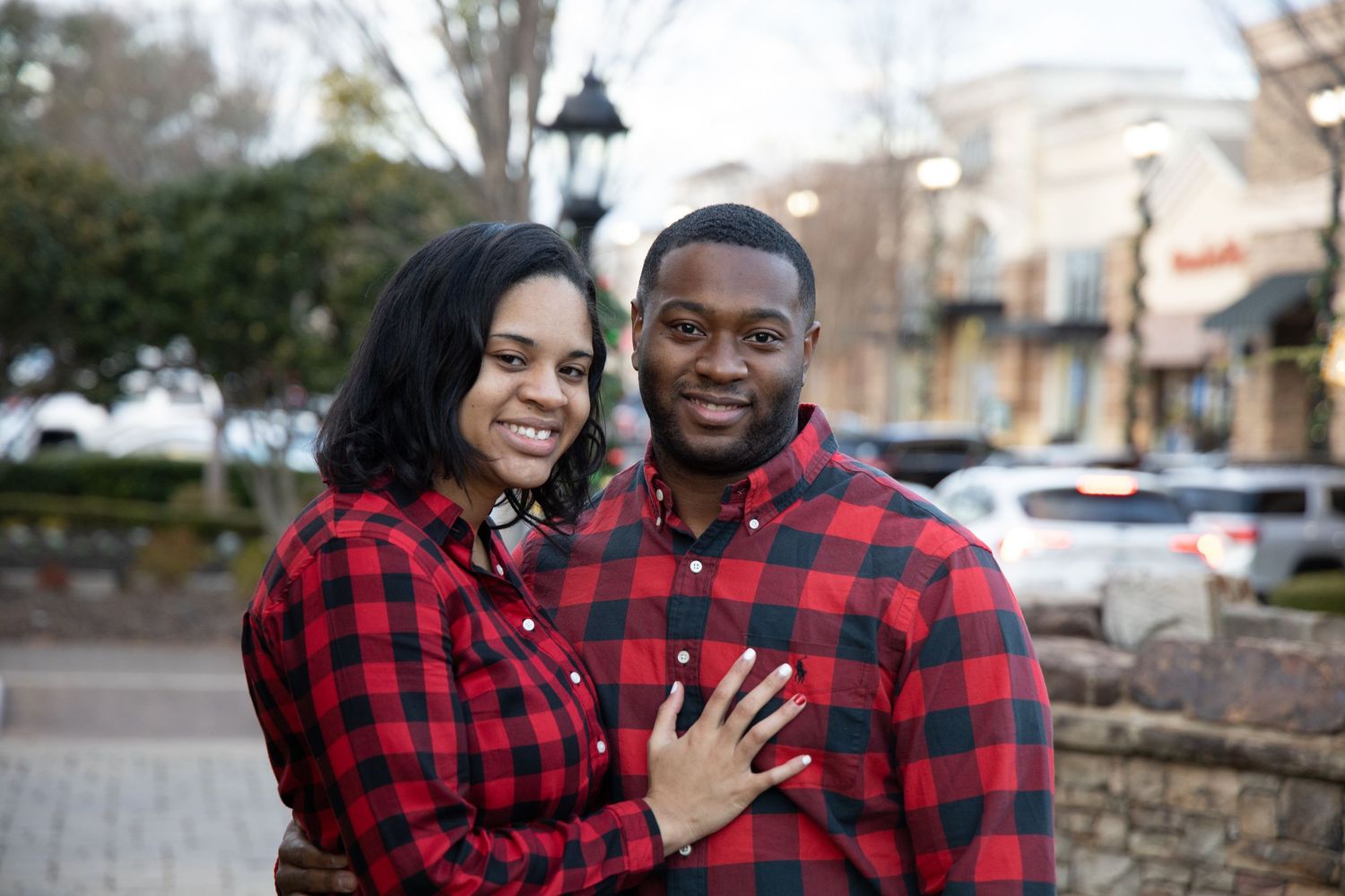 Couple wearing matching red plaid shirts pose together outdoors.