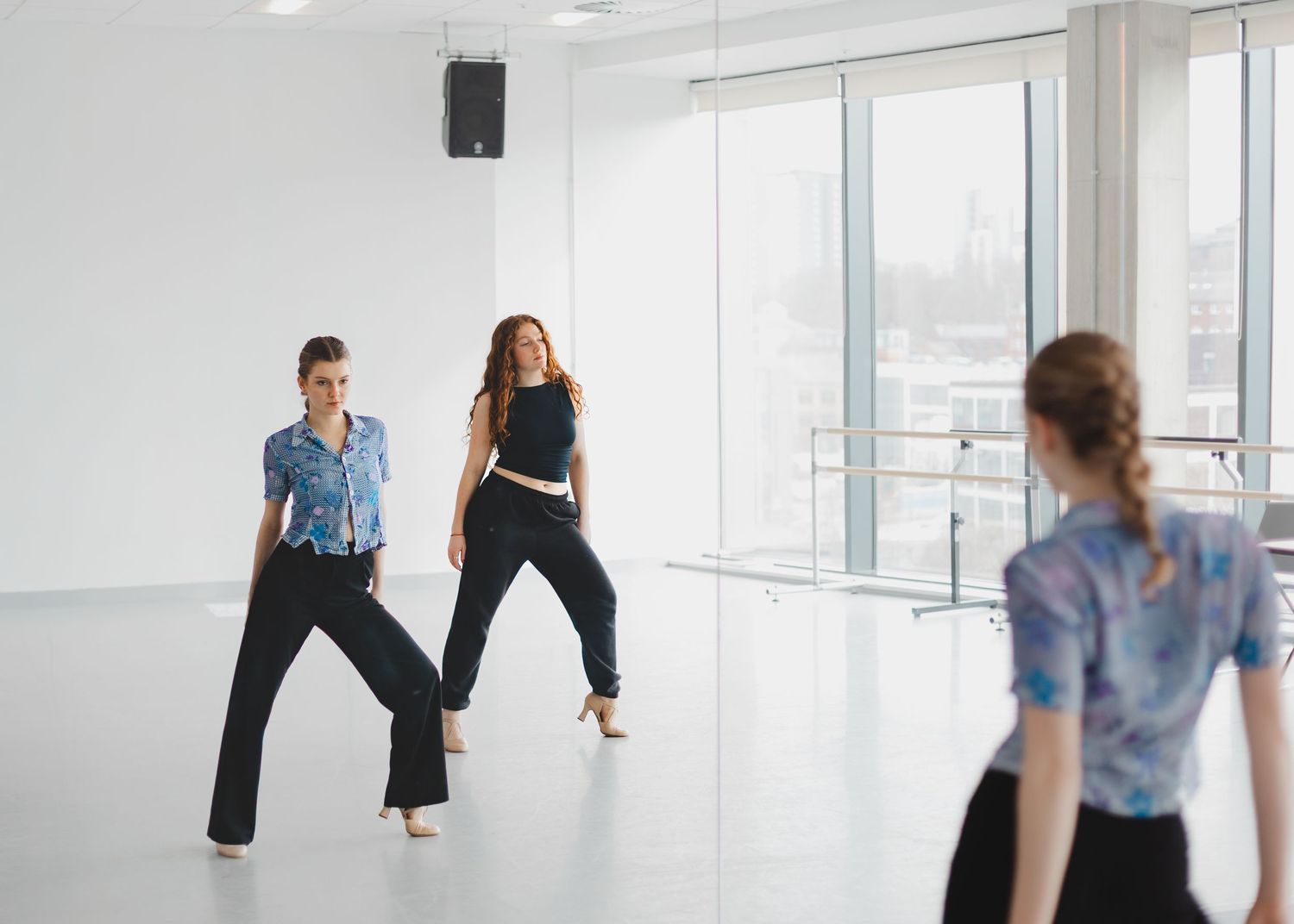 Dancers rehearsing choreography in a minimalist white dance studio space.