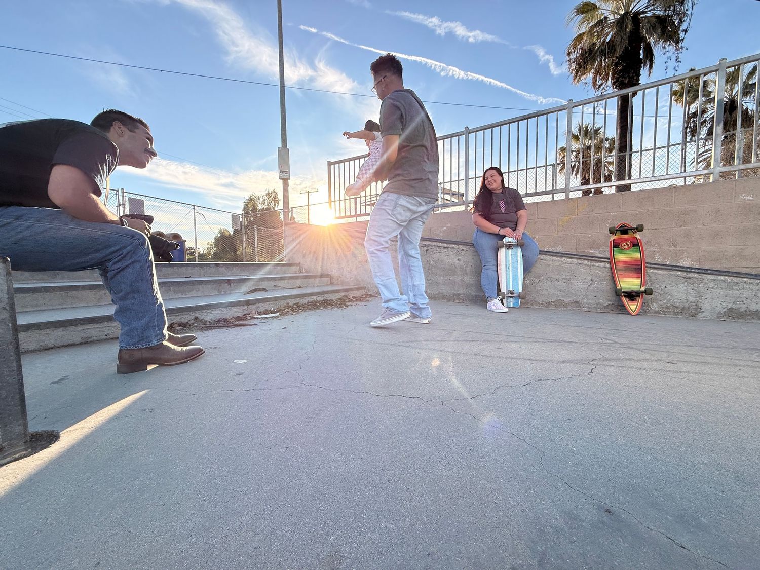 In a skate park with 1 photographer, 2 parents and their 1 baby. They are getting ready to pose for a photoshoot.
