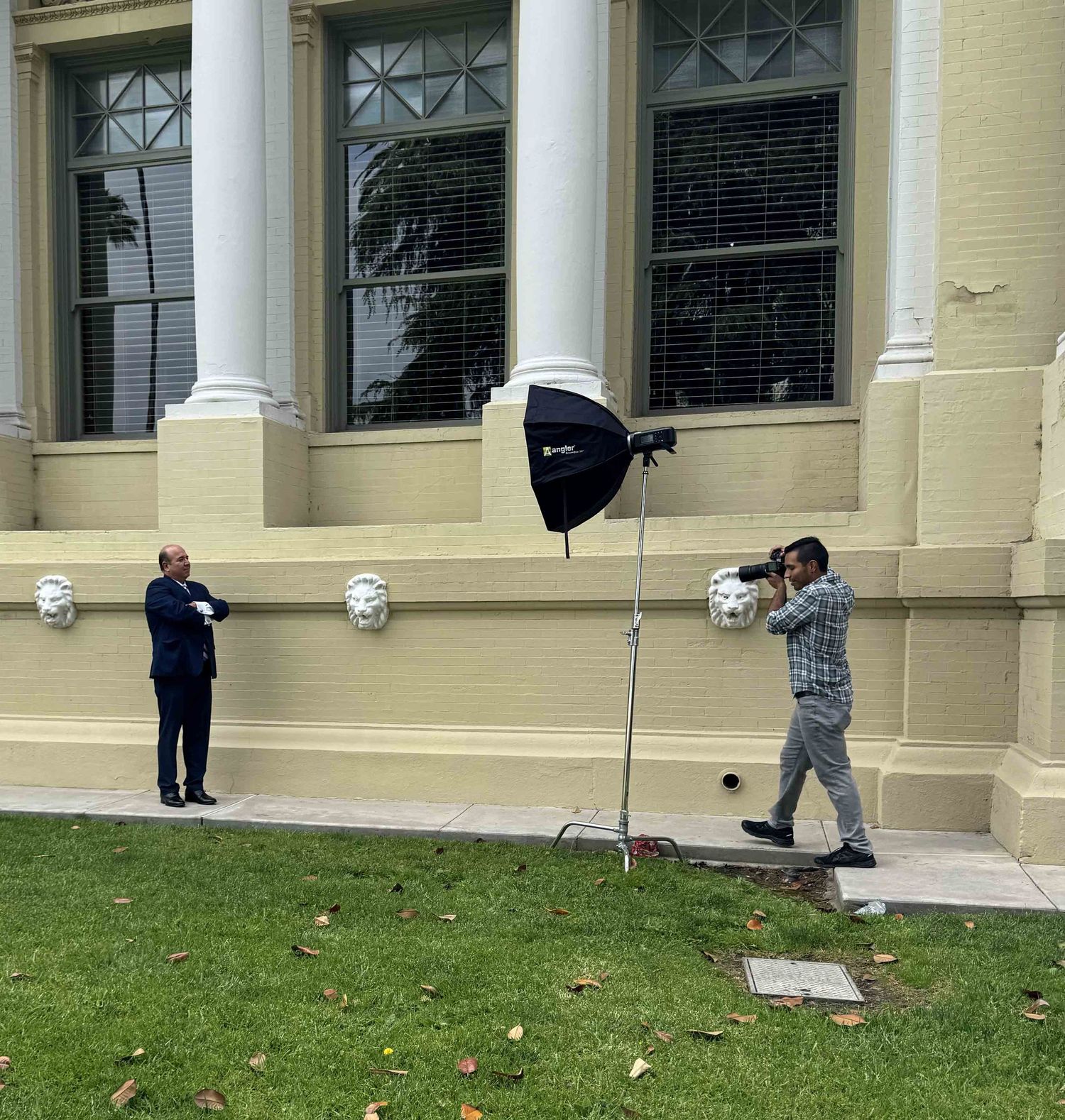 A lawyer posing for a portrait with a photographer aiming his camera for a shot. There's a light stand in between in the two.