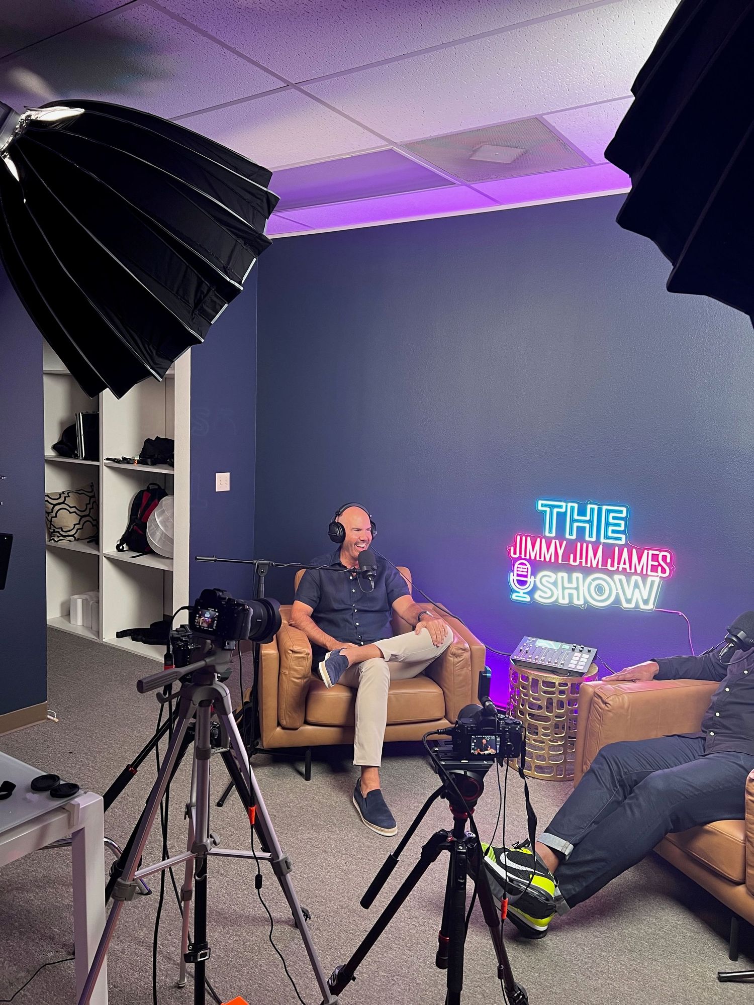 Behind-the-scenes of The Jimmy Jim James Podcast Show. Two men sitting on a couch and two cameras are in front of them.