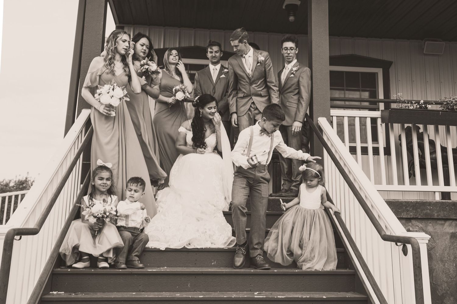 Wedding party poses on outdoor staircase in black and white photo with bridesmaids, groomsmen, and flower girls.