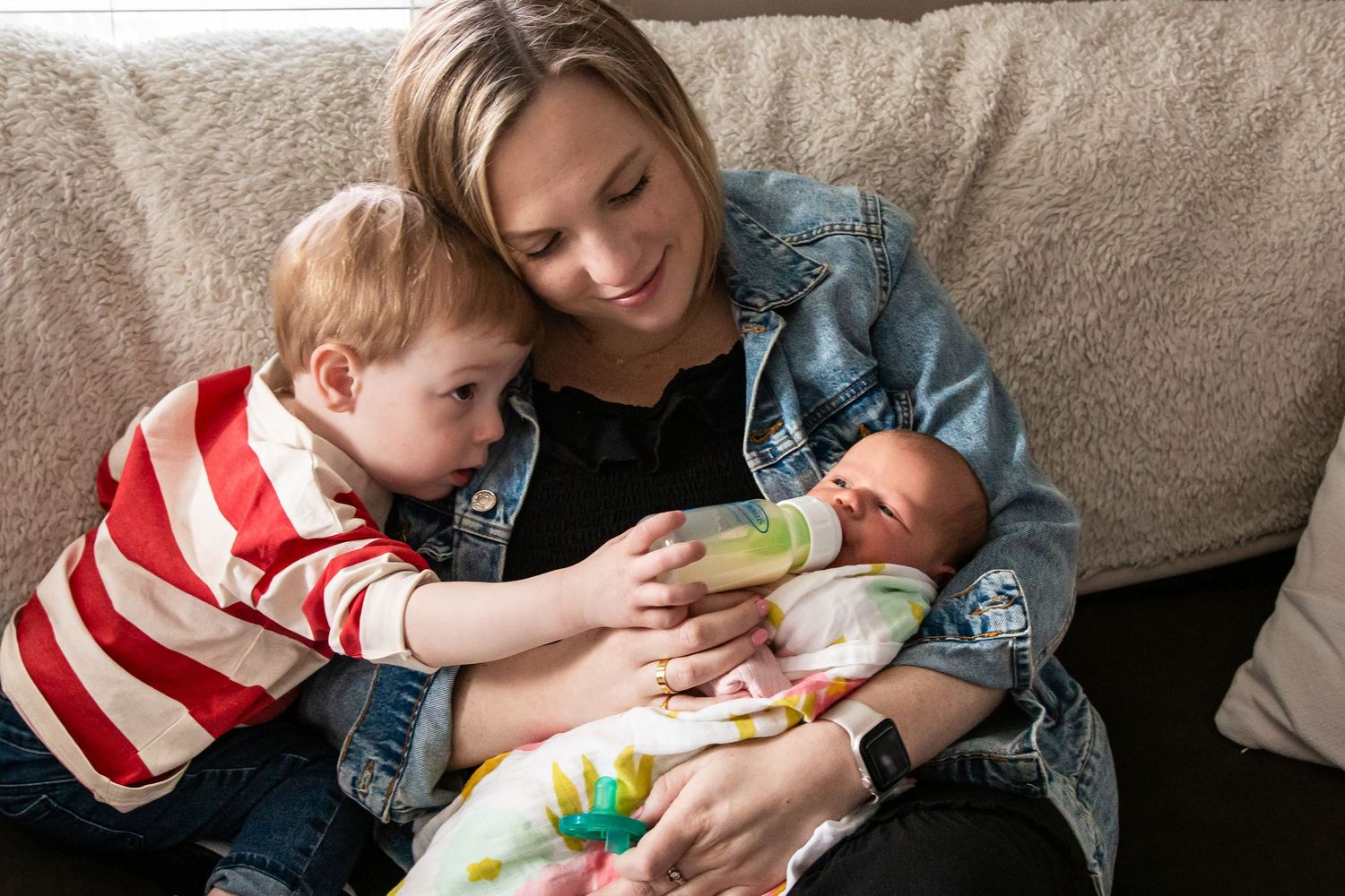 Mother sitting with toddler and newborn baby on a couch in a casual home setting.