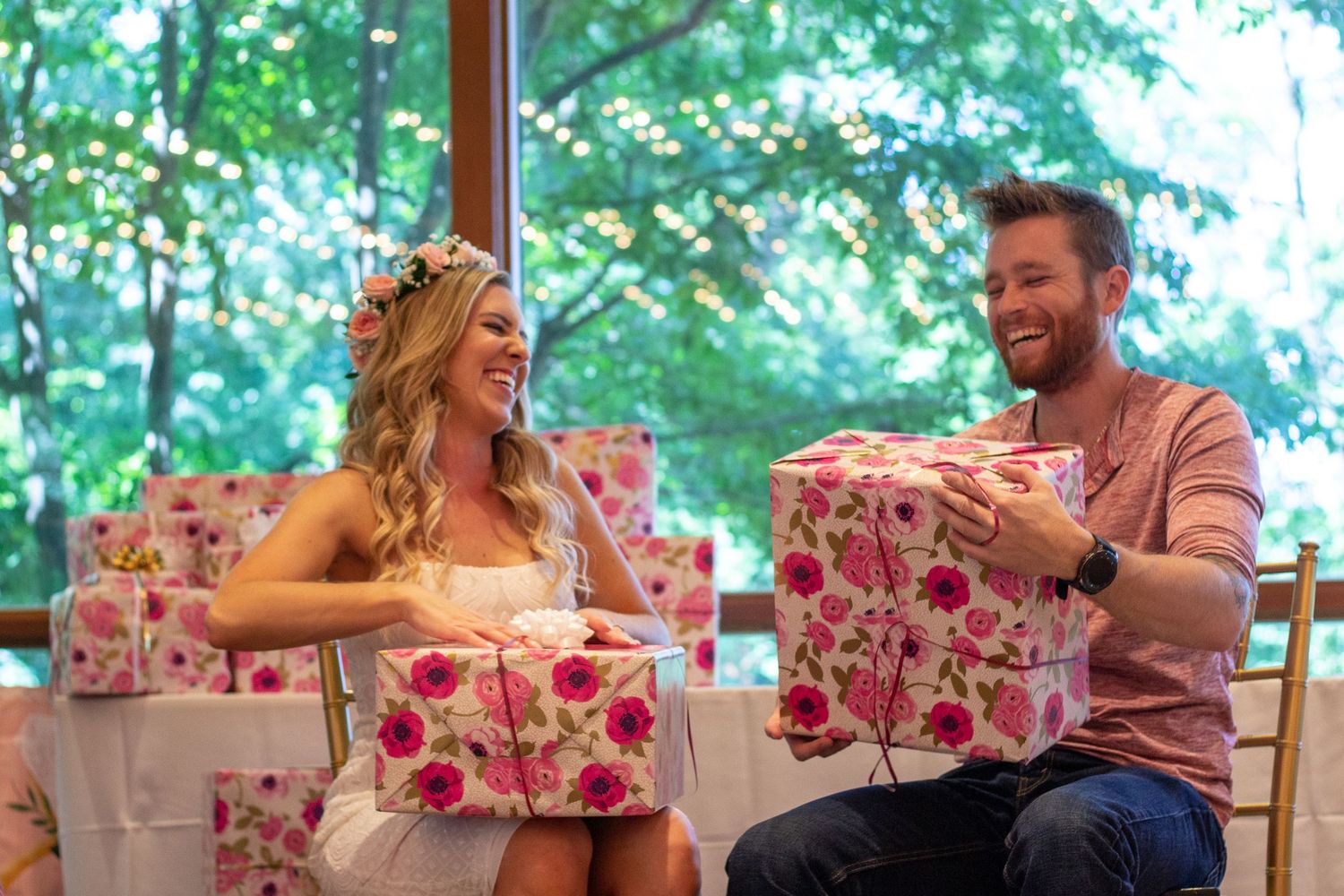 Smiling couple opens floral wrapped gifts together at a bright indoor celebration event.