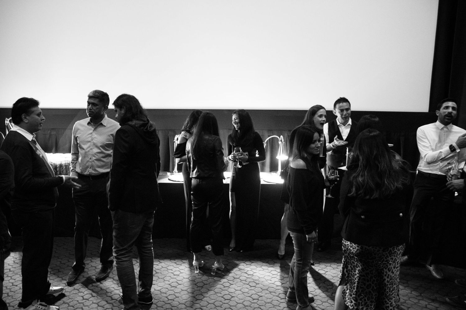 Black and white photo of elegantly dressed guests mingling at an indoor cocktail reception.