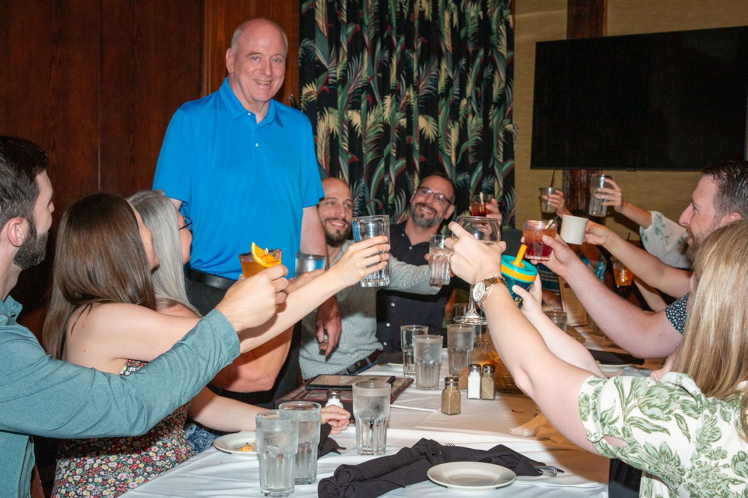 Group of friends raises colorful cocktails in a toast at a restaurant dinner celebration.