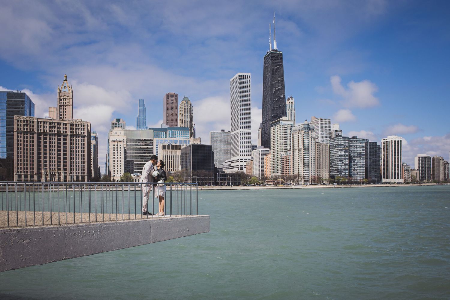 A couple shares a romantic kiss on a waterfront pier with the stunning Chicago skyline in the background.