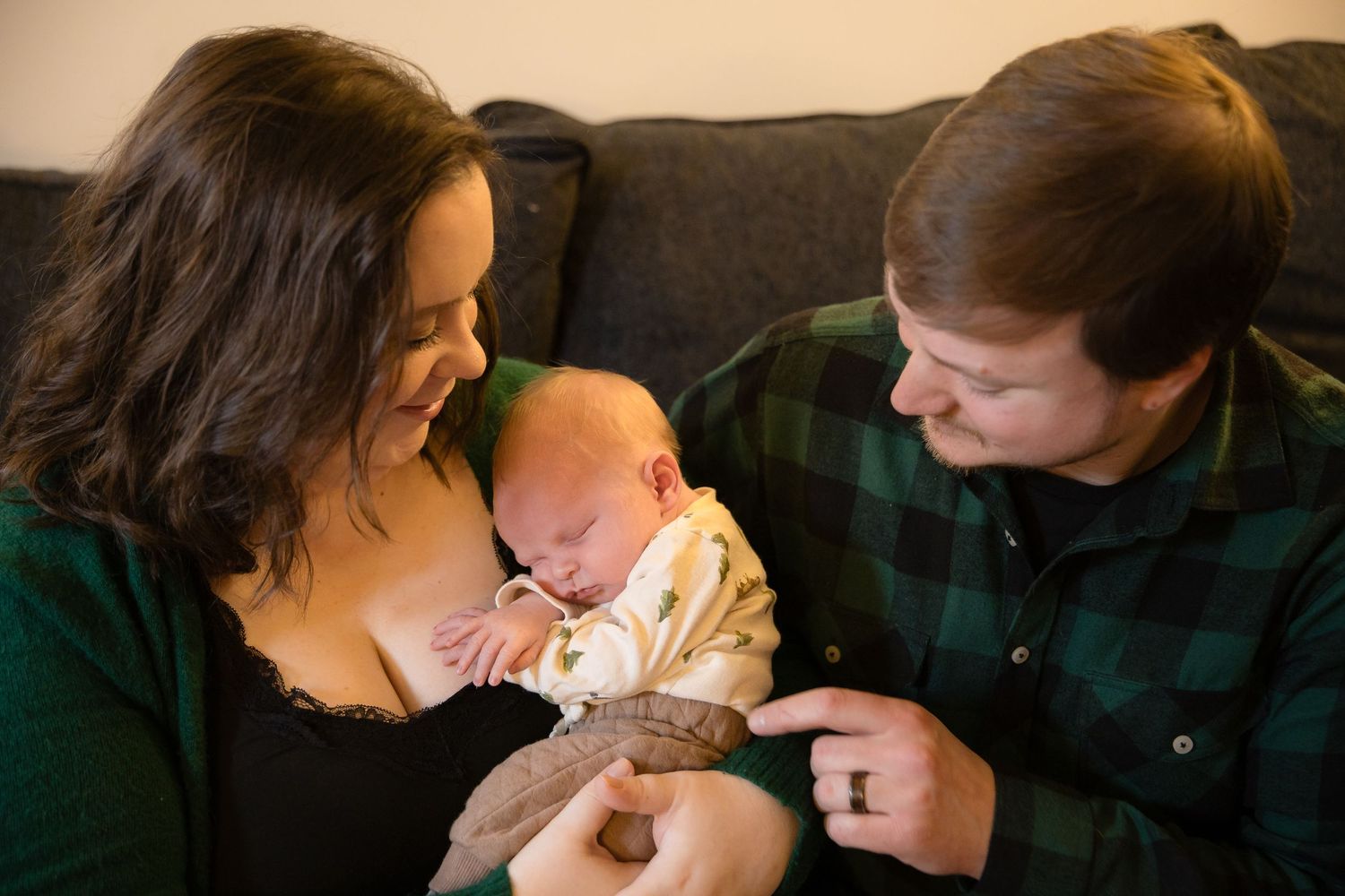 Happy new parents smiling and bonding with their newborn baby on a cozy living room couch.