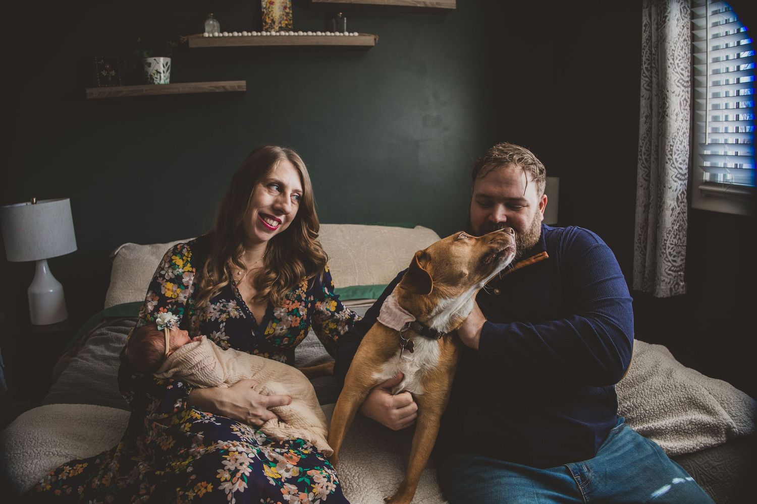 Happy couple laughing with their dog on a cozy couch in a modern living room.