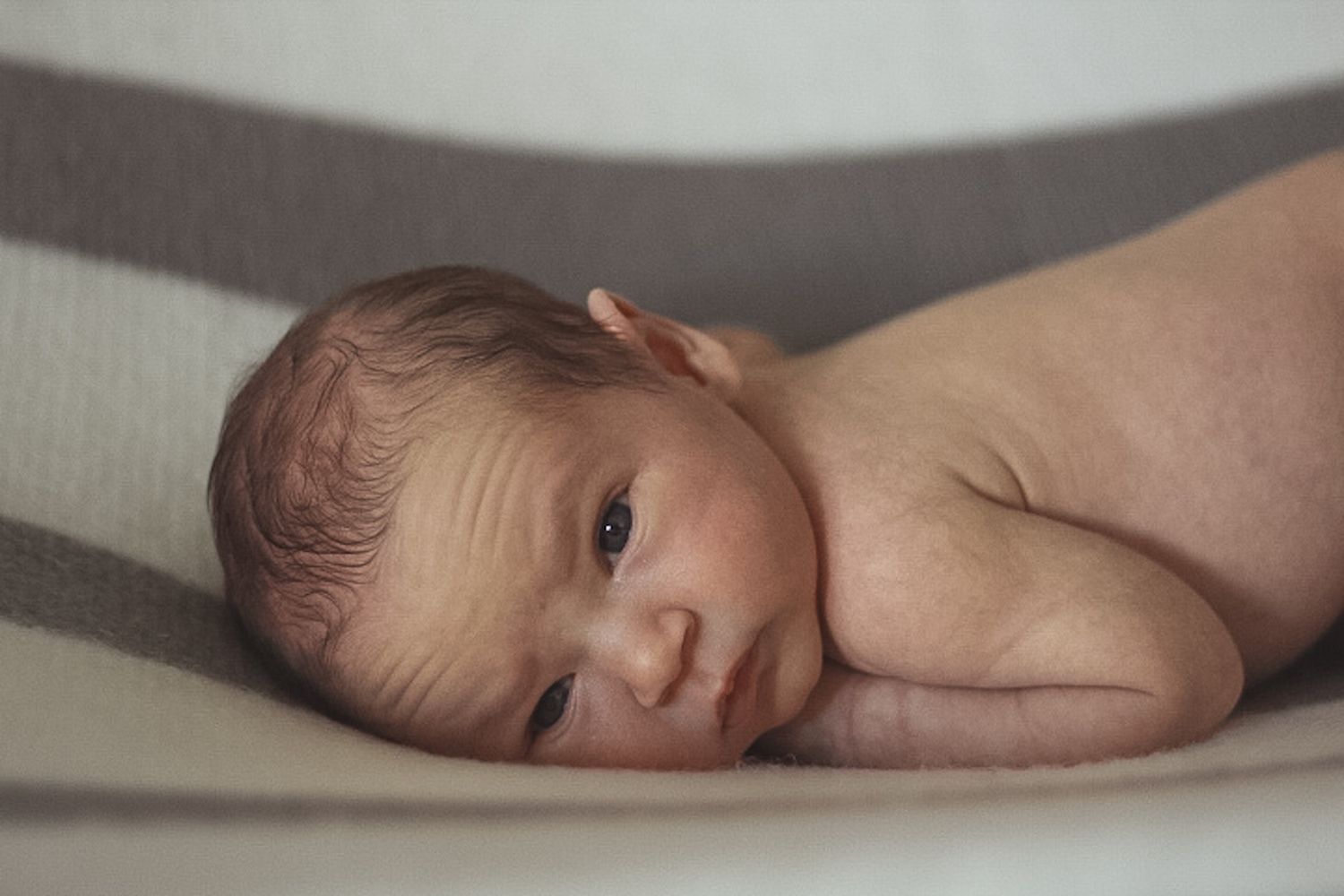 Awake newborn baby lying on striped blanket, looking up with curious wide eyes.