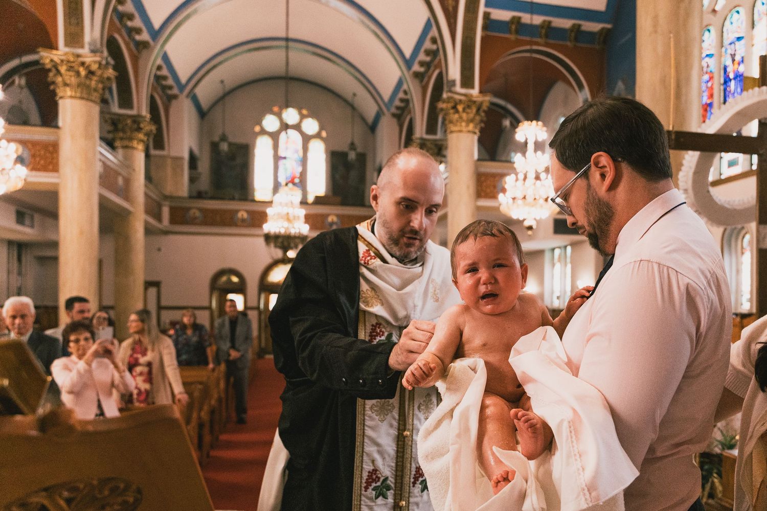 Orthodox priest baptizing a baby held by father in a beautiful church during a christening ceremony.
