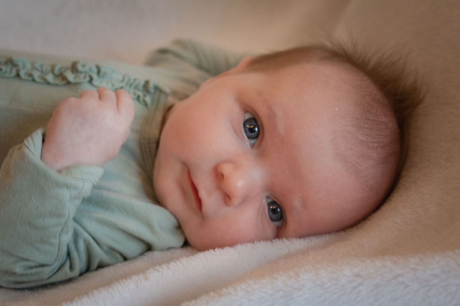 Close-up portrait of an alert newborn baby with blue eyes in a soft green outfit.