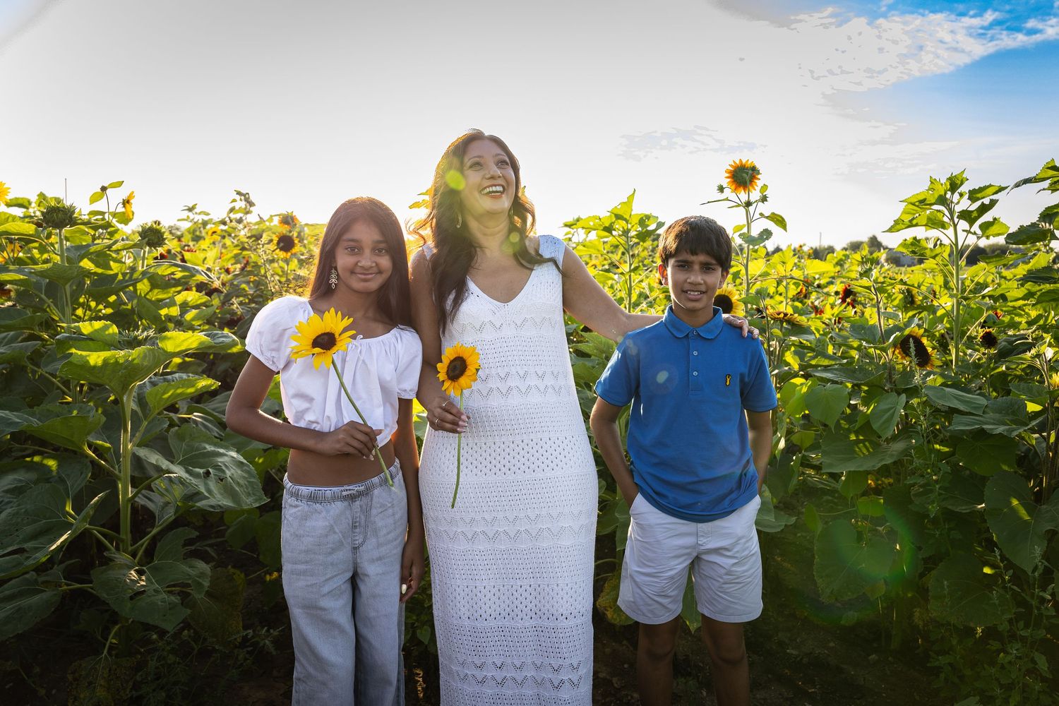 Mother and two children standing in a vibrant sunflower field on a bright sunny day.