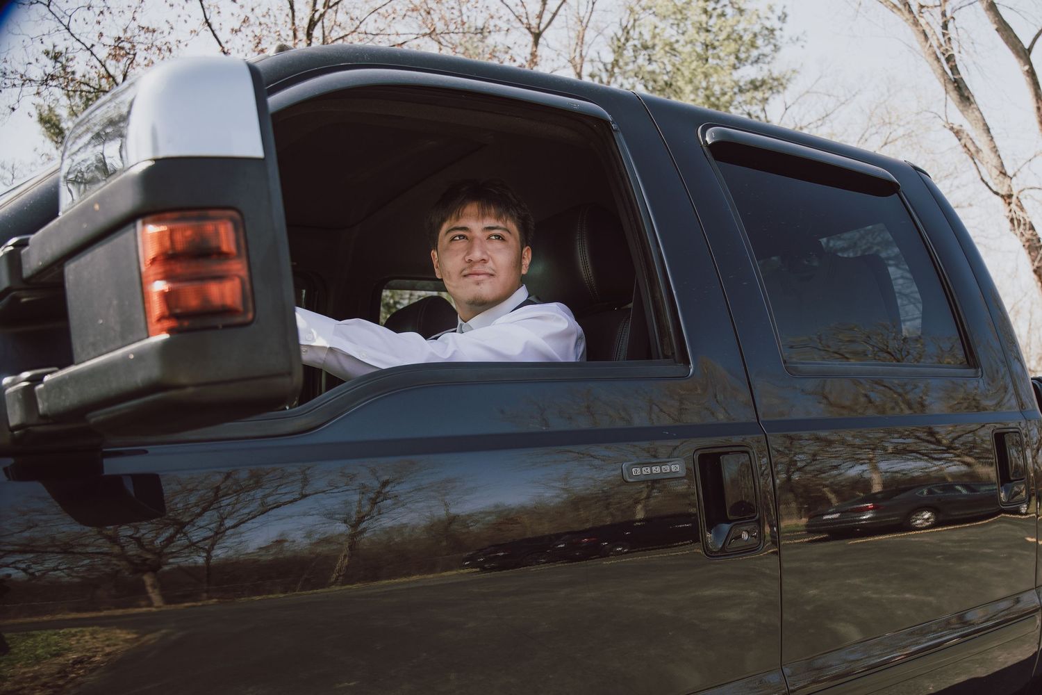 Young man sitting in driver seat of black pickup truck, smiling through open window on a sunny day.